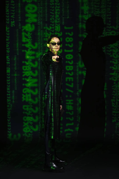 Nő pisztollyal öltözött mátrix stílusban sötét háttér - Fotó, kép