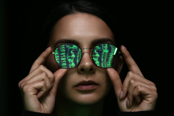 Femme avec reflet de code matrice dans ses verres teintés sur fond sombre - Photo, image