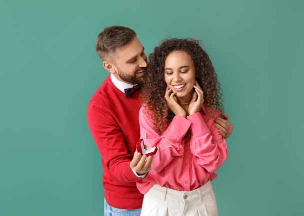 Junger Mann macht seiner Freundin auf farbigem Hintergrund einen Heiratsantrag - Foto, Bild