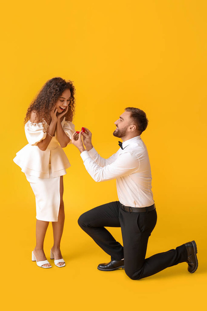 Young man proposing to his girlfriend on color background - Фото, изображение
