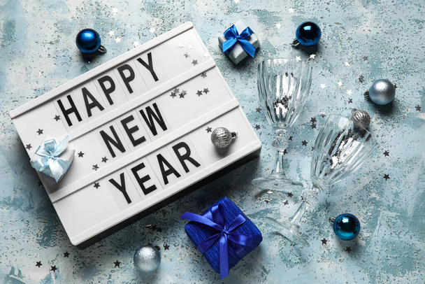 Board with text HAPPY NEW YEAR, glasses, gift boxes and Christmas decor on color background - Фото, зображення