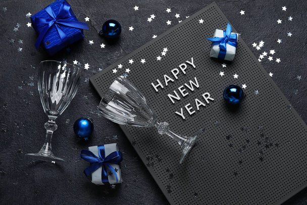 Yeni Yıl kutlu olsun yazılı pano, hediye kutuları, gözlükler ve karanlık arka planda Noel dekoru - Fotoğraf, Görsel