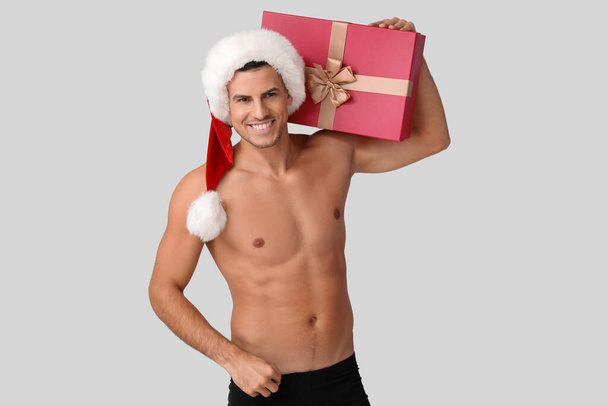 Sexy młody mężczyzna w Santa kapelusz, bielizna i z prezentem świątecznym na jasnym tle - Zdjęcie, obraz