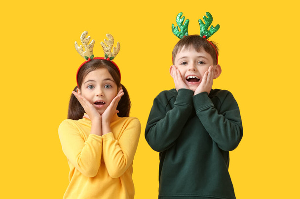 Surprised little children with reindeer horns on color background - Photo, Image