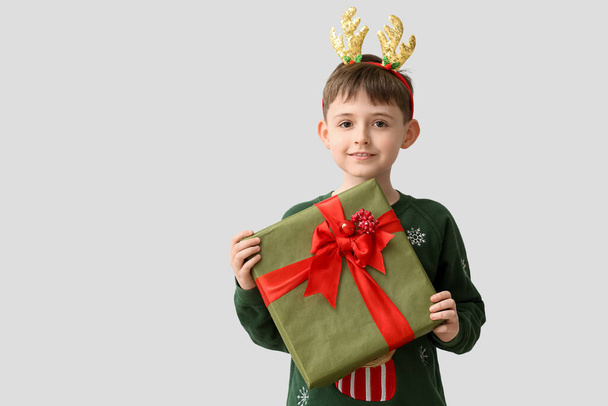 Funny little boy with reindeer horns and Christmas gift on light background - Foto, imagen