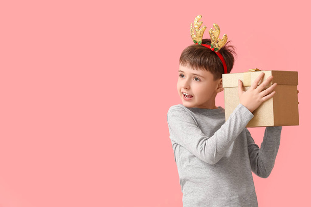 Funny little boy with reindeer horns and Christmas gift on color background - Foto, imagen