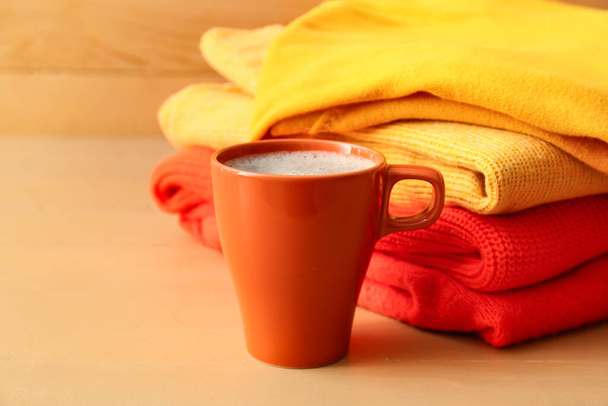 Pila de diferentes suéteres acogedores y taza de café sobre fondo de madera - Foto, Imagen