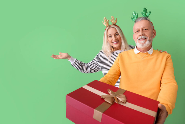 Glückliches reifes Paar mit Weihnachtsgeschenk auf farbigem Hintergrund - Foto, Bild