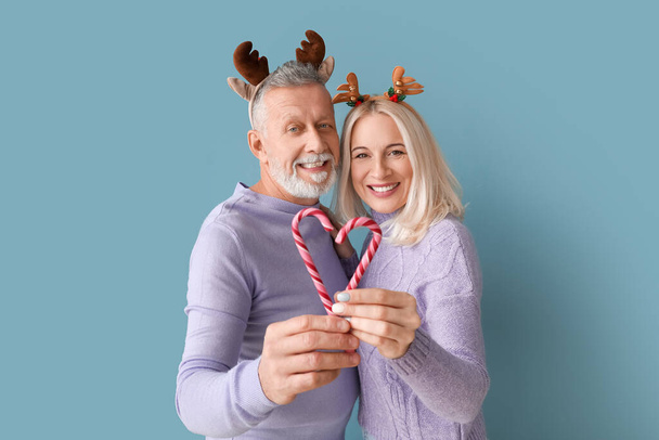 Glückliches reifes Paar mit Hirschhörnern und Zuckerstangen auf farbigem Hintergrund - Foto, Bild