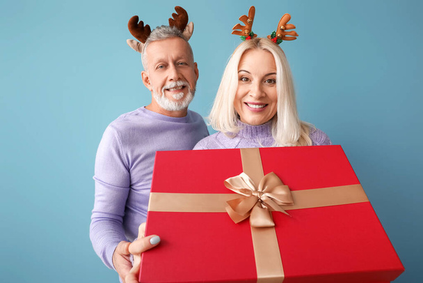 Happy mature couple with Christmas gift on color background - Foto, Imagen