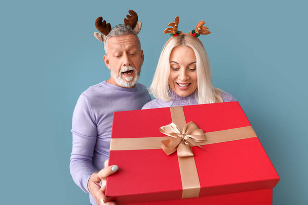 Happy mature couple with Christmas gift on color background - Photo, Image