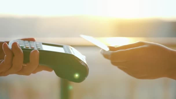 NFC luottokorttimaksu. Nainen maksaa kontaktittomalla luottokortilla NFC-teknologialla. Langaton rahansiirto. Kortti kone miehen kädessä auringonvalossa tausta - Materiaali, video