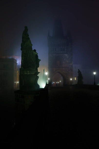 Street lamps and light from them on the old stone Charles Bridge in the night fog and silhouettes of figures - Foto, afbeelding