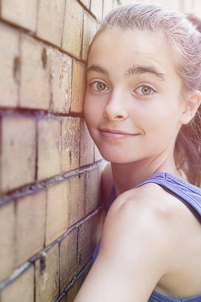 портрет усміхненої дівчини-підлітка, що спирається на цегляну стіну
 - Фото, зображення