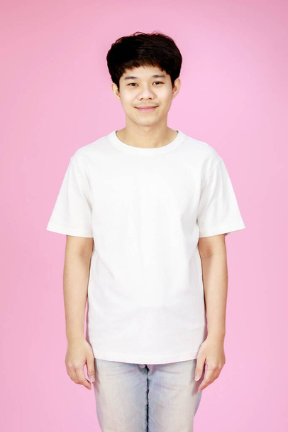 portret studio strzał z Azji młody przystojny szczęśliwy nastolatek krótkie włosy mężczyzna model w casual strój biały koszula i dżinsy stojąc samotnie uśmiechnięty patrzeć w aparat fotograficzny na różowym tle. - Zdjęcie, obraz