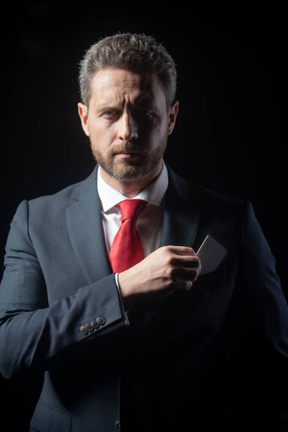 Portrait of an elegant handsome business man isolated on black. Handsome thoughtful middle-aged businessman with credit card in suit posing against a black background with copy space. - Foto, Bild
