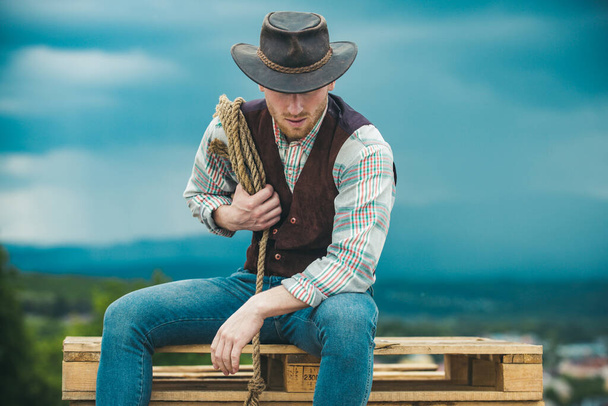 American cowboy man. Cowboy with lasso rope on sky background. Brutal western guy. - Fotó, kép