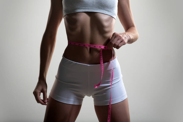 Slim young woman measuring her thin waist. - Valokuva, kuva