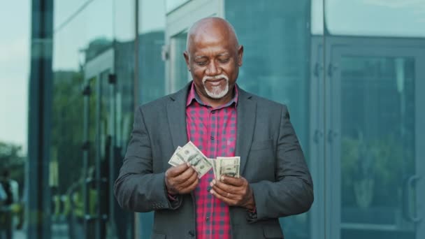 Ώριμος άντρας με ένα σωρό δολάρια που μετράει χαρτονομίσματα. Χαρτονομίσματα σε αντρικά χέρια. Επιτυχία και πλούτος επιχειρηματική έννοια. Ευτυχισμένος Αφροαμερικάνος ηλικιωμένος συνταξιούχος μετράει το ποσό των χρημάτων για να αγοράσει - Πλάνα, βίντεο
