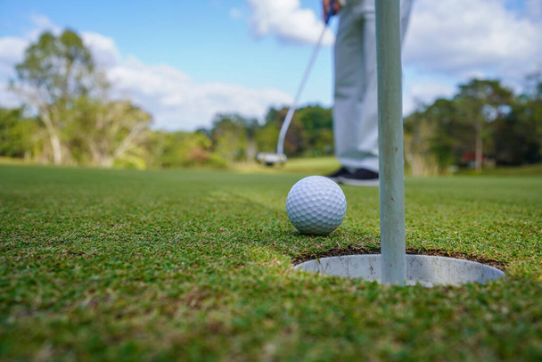 Golfer zet bal op de groene golf, lens flare op zonsondergang 's avonds tijd. Golfer actie te winnen na lange putting golfbal in het gat.                                - Foto, afbeelding