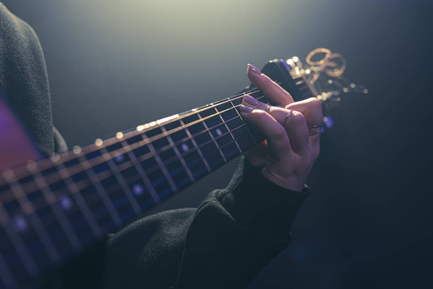 Μια γυναίκα που παίζει ακουστική κιθάρα σε ένα σκοτεινό δωμάτιο με θολούρα. - Φωτογραφία, εικόνα