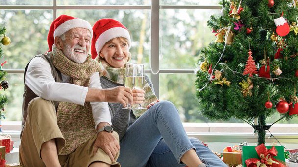 Glücklich reife Frau und alter Mann begutachten Geschenk, während sie auf Teppich zwischen geschmückten Weihnachtsbäumen gegen Fenster zu Hause sitzen - Foto, Bild