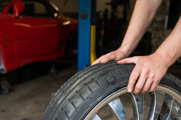 An auto mechanic holds a wheel of a car. Change of car tires according to the season - Fotoğraf, Görsel