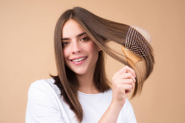 Girl combing hair. Beautiful young woman holding comb straightened hair. Attractive smiling woman portrait with comb. - Фото, зображення
