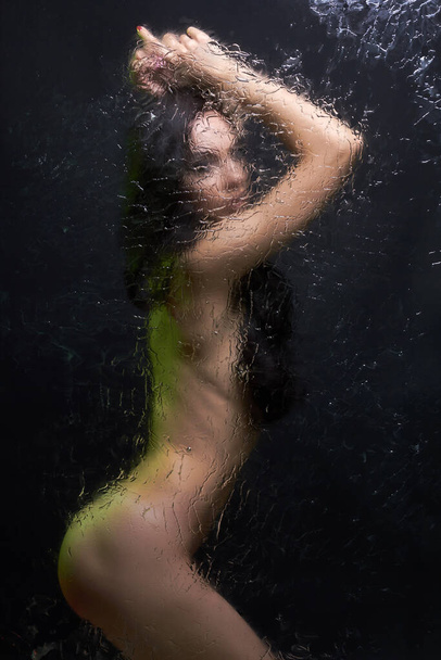 Голая женщина за мокрым стеклом. Сексуальная красивая девушка в душевой кабине. яркие огни - Фото, изображение