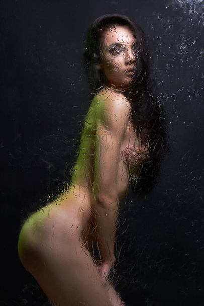Nude woman behind wet glass. Sexual Beautiful Girl in shower cabin. color bright lights - Фото, изображение