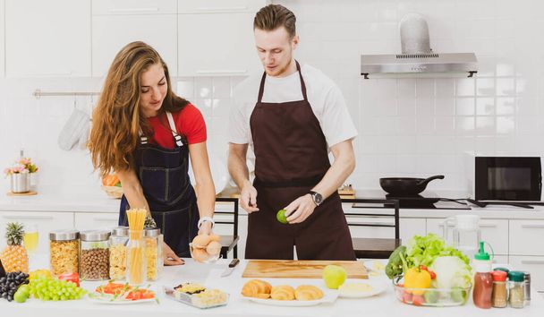 Mies ja nainen viettävät aikaa yhdessä modernissa keittiössä. He leikkaavat ja valmistavat hedelmiä ja vihanneksia ateriaa varten. - Valokuva, kuva