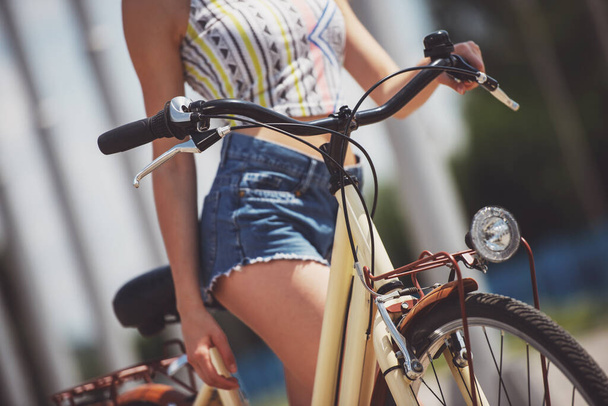 Γυναίκα σε γυαλιά ηλίου με ποδήλατο στέκεται στο δρόμο της πόλης. Κινηματογράφηση σε πρώτο πλάνο. - Φωτογραφία, εικόνα