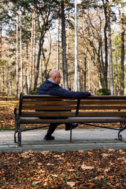 An adult man sits on a bench in an autumn park. Loneliness, relaxation and nostalgia. Back view. Vertical. - Foto, immagini