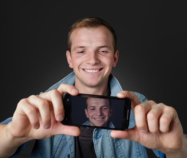 mladý muž vzít vlastní fotografie s jeho mobilung man tagit en egen bild med sin mobiltelefon. - Fotografie, Obrázek
