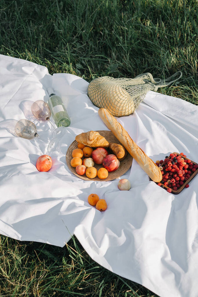 Apples, croissants, baguettes and fruits lie on a picnic tablecloth in the field - Fotoğraf, Görsel