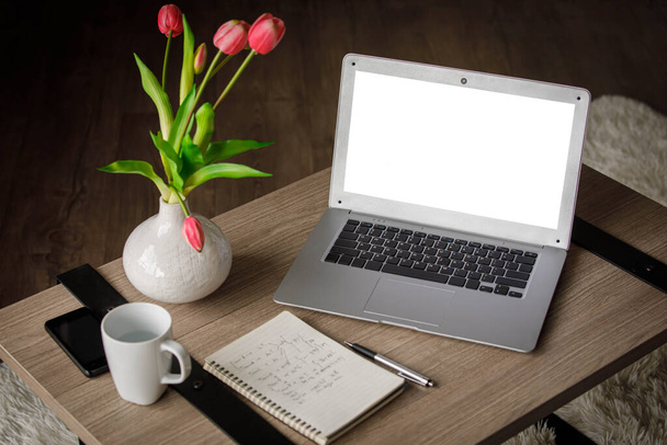 Da sopra blocco note e netbook moderno con schermo bianco posto sul tavolo vicino al vaso con tulipani e tazza con acqua a casa - Foto, immagini