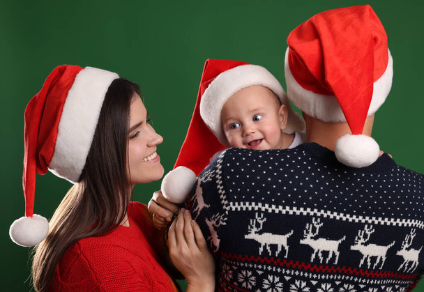 Happy couple with cute baby in Christmas outfits and Santa hats on green background - 写真・画像