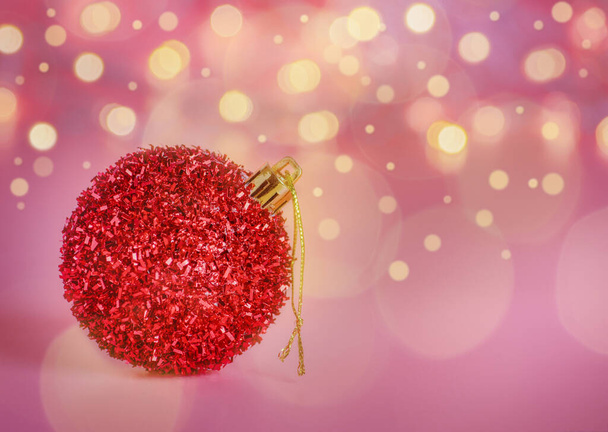 Κόκκινη χριστουγεννιάτικη μπάλα σε ένα εορταστικό ροζ φόντο με φώτα defocused. Αντιγραφή χώρου. - Φωτογραφία, εικόνα