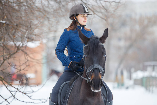 Portrait of teenage girl riding raven horse in winter - Foto, imagen