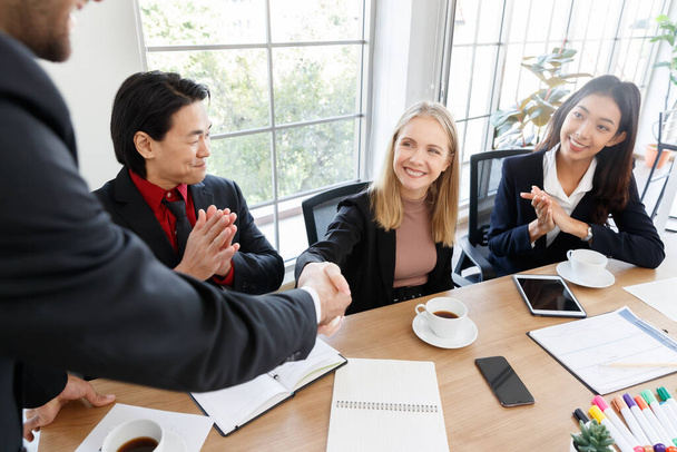 Crop anonymous man shaking hand of optimistic businesswoman sitting near multiracial coworkers at table with documents during meeting in conference room - Photo, Image