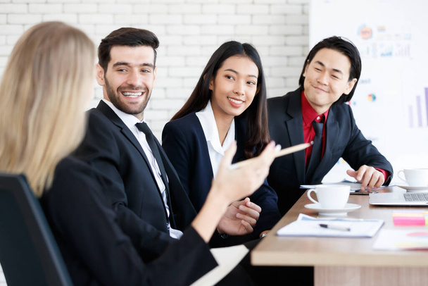 Group of positive multiracial coworkers in elegant clothes sitting at table with documents while working together in modern conference room - Photo, Image