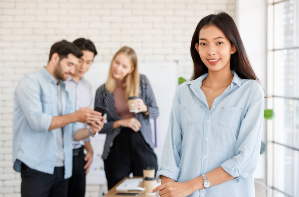 Positive Asian female manager standing near group of multiracial coworkers discussing project while working together in light conference room - Photo, image