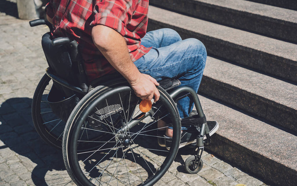 Молодий чоловік з фізичною вадою в інвалідному візку перед сходами
 - Фото, зображення
