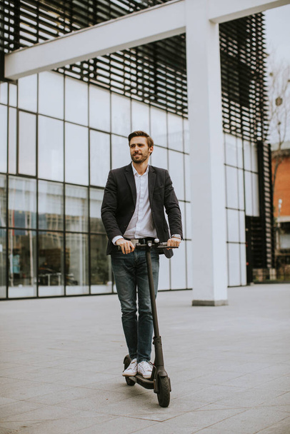 İş görüşmesindeki bir ofis binasının önünden elektrikli scooterla geçen sıradan giysili yakışıklı bir iş adamı. - Fotoğraf, Görsel