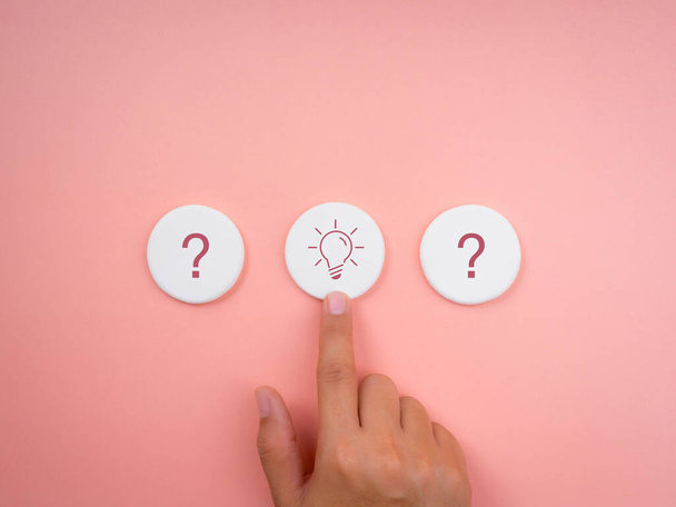 Die Lösung, die kreative Idee und Innovation, die Suche nach Erfolgskonzepten, minimaler Stil. Glühbirne und Fragezeichen-Symbol auf weißem, rundem Schwamm mit ausgewählter Hand auf rosa Hintergrund. - Foto, Bild