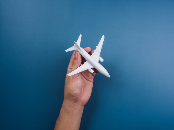 Hand holding white plane toy model on a blue background, top view, minimal style. White airplane, flat lay design. Flight, travel concept. - Фото, изображение