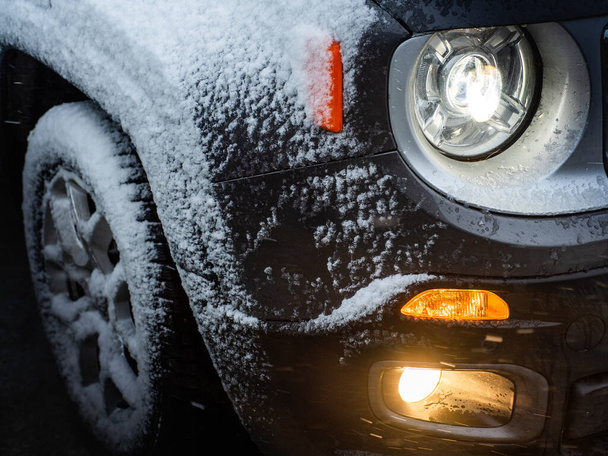 Чёрный полноприводный автомобиль с включённым светом на зимней дороге,  - Фото, изображение