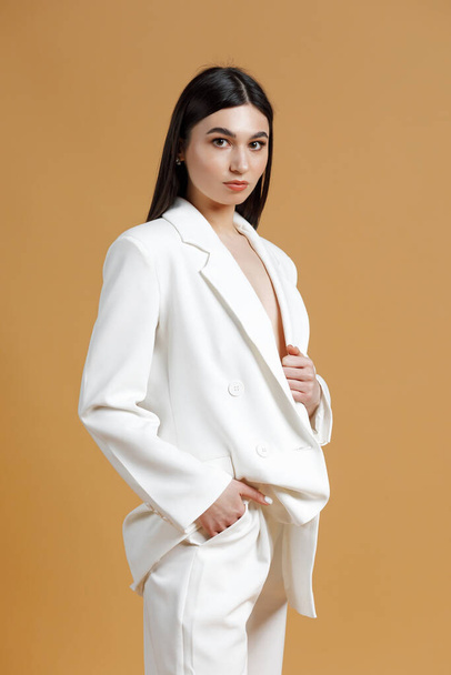 Portrait of a young pretty woman wearing a white suit while posing in a studio with orange background - Photo, Image