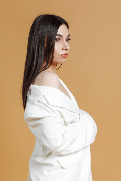 Фото молодой красивой модели в белом костюме, позирующей в студии с оранжевым фоном - Фото, изображение