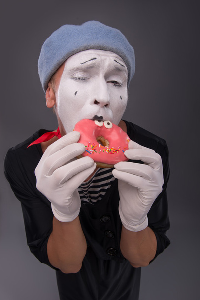 Portrait of handsome male mime eating a tasty pink donut with fu - Foto, Bild